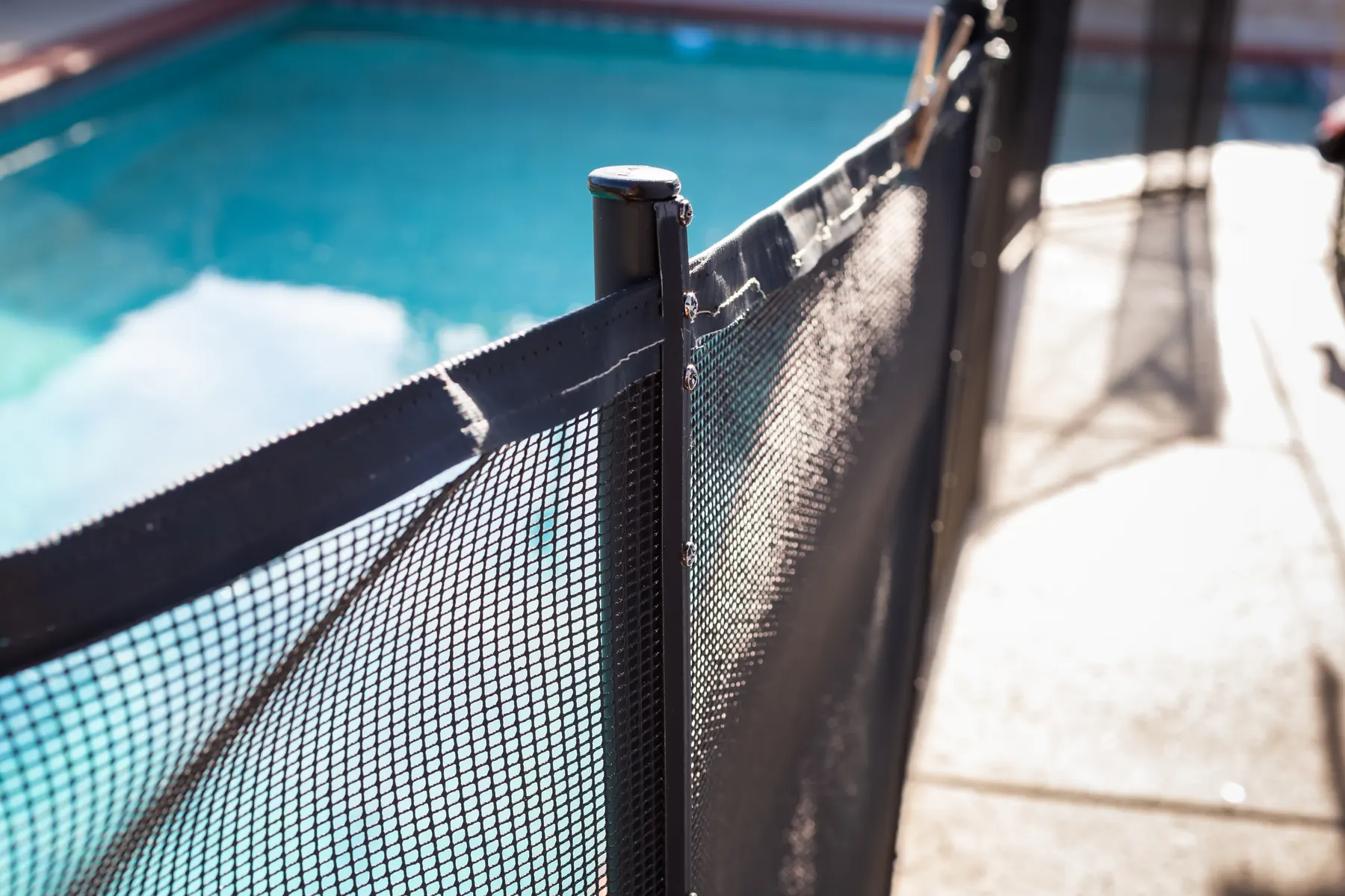 Close-up of a mesh pool safety fence post beside a residential backyard pool, the kind of barrier Arizona's pool fence law regulates